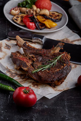 Tomahawk steak with vegetables and a knife on the table. Grilled meat with grilled vegetables and...