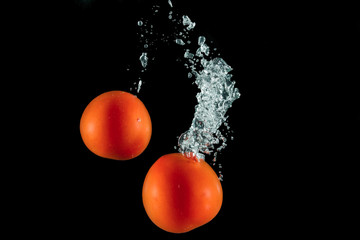 tomatoes under water with splashes on a black background