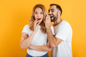 Image of attractive couple man and woman in basic t-shirts whispering secrets or gossips to each...