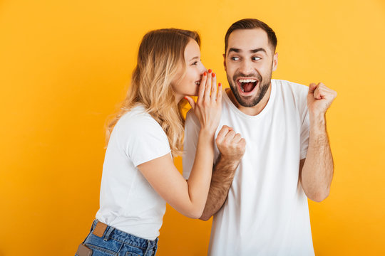 Image of ecstatic couple man and woman in basic t-shirts whispering secrets or gossips to each other