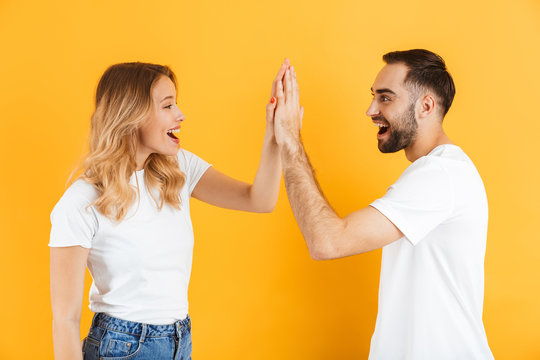 Image of delighted couple man and woman smiling and gesturing high five while looking at each other
