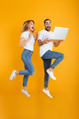 Full length image of excited couple man and woman rejoicing while holding laptop together