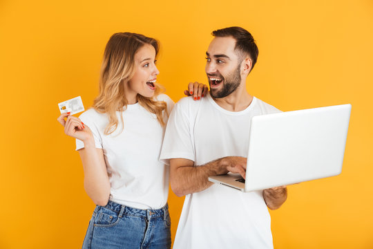 Image of beautiful couple man and woman expressing surprise together while holding laptop and credit card