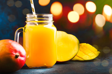 Mango juice or cocktail in glass jar with fresh fruit on blue tropical background, copy space, selective focus