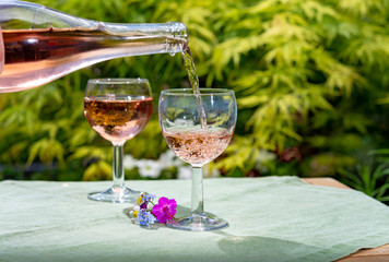 Waiter pouring cold rose wine in glasses in summer sunny day in blossoming garden