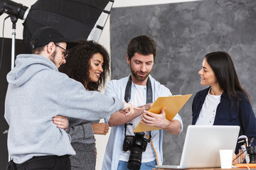 Portrait of cheerful multiethnic people men and women talking while photographer shooting model in studio