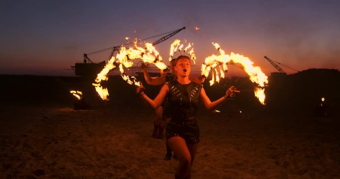 Fire show three women in their hands twist burning spears and fans in the sand with a man with two flamethrowers in slow motion.