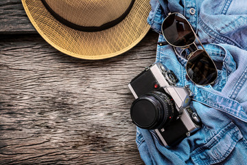 Travel and vacations concept ,old retro film analogue camera, jeans, hat, and sunglasses, traveler's accessories on wooden table style vintage
