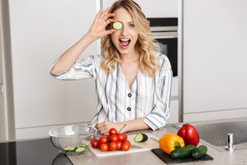 Happy young beautiful woman posing at the kitchen at home cooking.