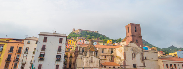 Panorama of the colorful town of Bosa along a river and hills in sunlight in spring