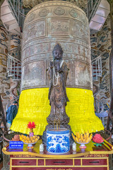 Big old metal bell with glued sheets with wishes and ancient statue in pagoda in Vietnam