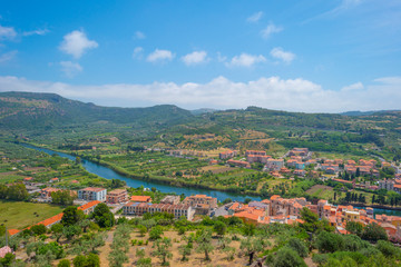 Panorama of the colorful town of Bosa along a river and hills in sunlight in spring