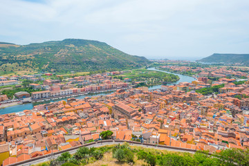 Fototapeta na wymiar Panorama of the colorful town of Bosa along a river and hills in sunlight in spring