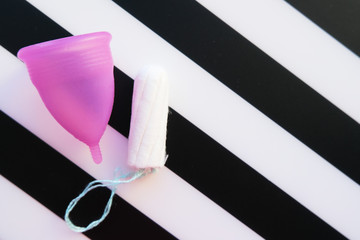 Reusable menstrual cup and tampon on striped black and white background, Concept female intimate hygiene period products and zero waste. Flat lay, minimalism, top view. copyspace.