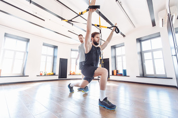 Male trainer teaches his student how to workout with suspended training system. Concept of strength training and work with the support of a coach