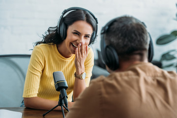selective focus of cheerful radio host laughing while recording podcast with colleague