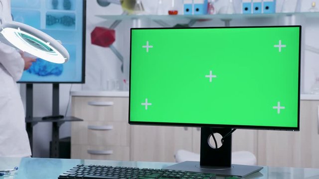 In modern high end medical office doctor walks in the background while a green screen PC is displayed on the glass desk