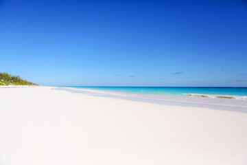 A pristine beach seen with perfect pink sand and bright blue sky and water. 