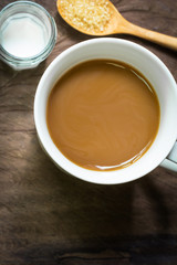 Cup of coffee with brown sugar and milk on wooden background