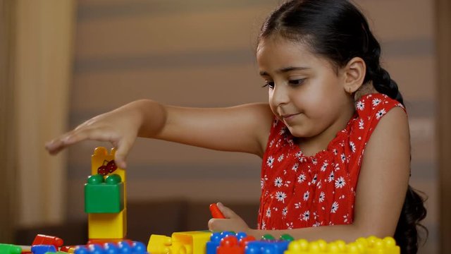 Charming cute Indian child girl playing at home with block colorful toys - childhood concept. Stock video of a little preschooler girl  playing and building a tower with blocks 