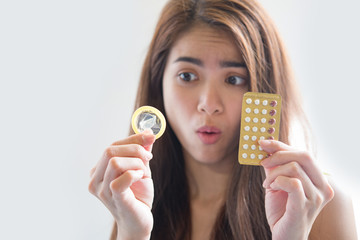 Young woman holding condom and contraceptive pills prevent pregnancy