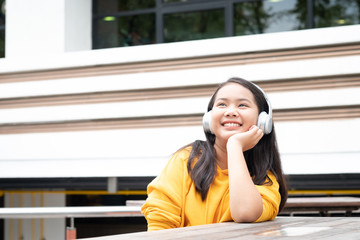 Happy smiling little girl listening to music in the park with her headphones