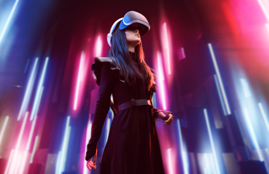 Beautiful woman in futuristic dress over dark background. Girl in glasses of virtual reality. Augmented reality, game, future technology, robots and people concept. VR. Neon light.