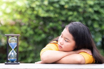 Little Asian girl is looking at the hourglass with feelings of loneliness