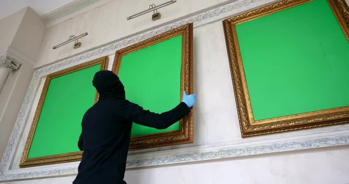 Male thief in mask stealing artwork from museum