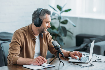 handsome radio host in headphones using smartphone while sitting at workplace