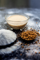 Hair growth remedy of rice flour water and fenugreek/coriander/parsley seeds powder on wooden surface and its paste in a glass bowl with some rice flour spread on the surface. Vertical shot.