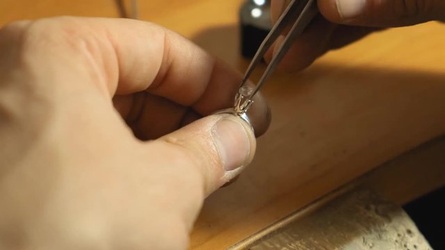 Close up view of puttin the gemstone into a crone of metal ring in jewellery slow motion
