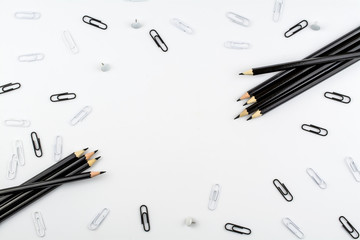 Black pencils and paper clips, white buttons and paper clips lie on a white background.