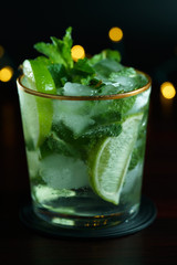 Macro shot of mojito served in a glass with gold rim. Dark wooden table, festive lights, high resolution