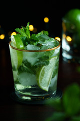 Mojito served in a glass with gold rim. Limes and mint in bokeh, dark wooden table, high resolution