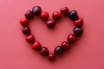 Heart made with cherries on a pink paper background. Top view, high resolution