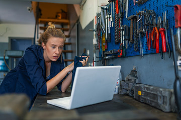 Female Mechanic. Female mechanic with laptop. Young female mechanic with laptop. Business woman at a factory. Craftswoman working using a laptop in the garage