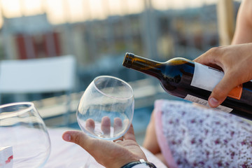 Pour red wine. Young man and girl with champagne and have fun outdoors. Hands holding a glass and a bottle of red wine. Close-up of the wine is poured into a glass.