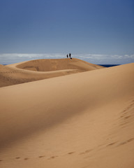 Fototapeta na wymiar Two people in the distance on top of one of the dunes in Maspalomas, Gran Canaria, Spain. 