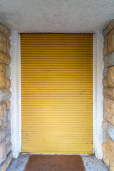 Background of bricks stone wall and closed yellow roll-up door