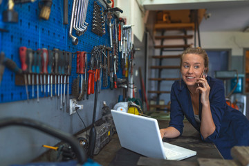 Mechanic in uniform is using a laptop in auto service. Mechanic typing on a laptop at the repair garage. Young female mechanic with laptop. Business woman at a factory.