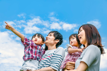 青空をバックに遠くを見つめ指さす4人家族。幸せ、希望、愛情、育児イメージ