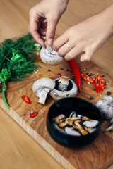 Photo of a preparation of ingridients such as musseles, red chilli peppers, fresh greens, mushrooms, broccoli with attractive woman hands on a wooden table