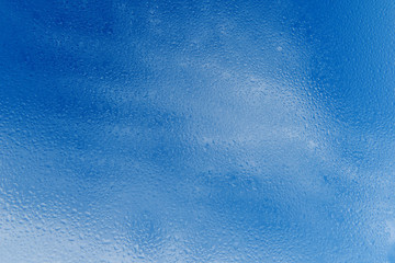 Transparent clean raindrops on the glass against the background of bright blue sky with clouds. Graphic resource, postcard, background, space for printing, copy space