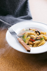 Photo of a fresh hot delicious italian fussili pasta with sea mussels, black olives, red chilli peppers and fresh greens on a white porcelain plate