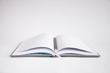 open notebook on the table. On the notebook is a black pencil. On a white background