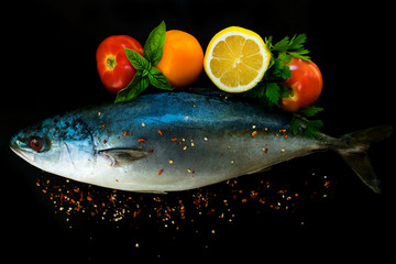  Fresh sea fish tuna in with vegetables and spices on a black background. Close-up.