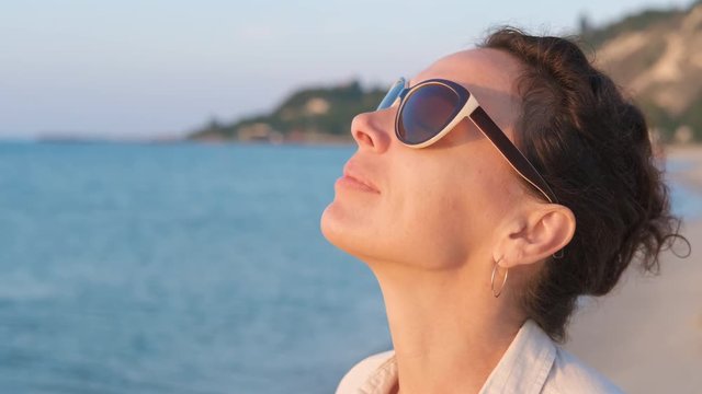 Woman in sunglasses enjoys the dawn. Nice woman in protective glasses on the seashore.