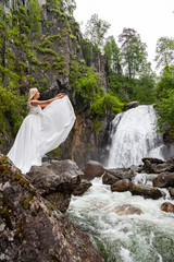 A young blonde girl in an elegant pose throws up hem of a boudoir dress in the mountains against a...