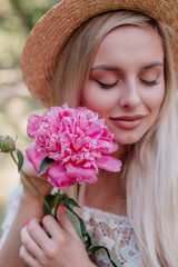 Portrait of a young blonde woman in straw hat with peony flower in outdoor.